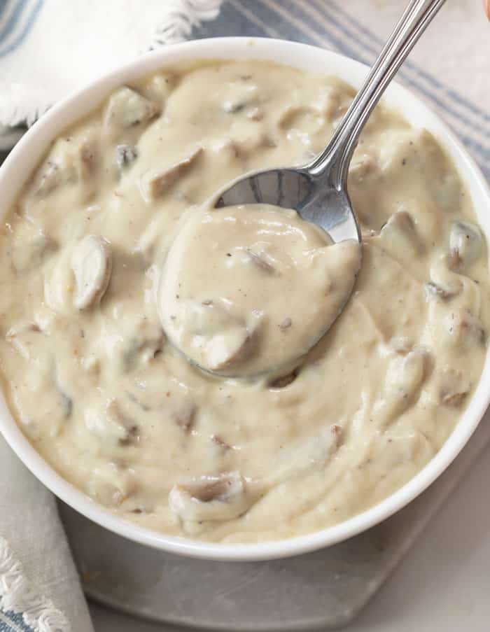 A white bowl filled with condensed cream of mushroom soup with a spoon in it.