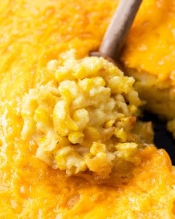 A wooden spoon scooping up Corn Casserole from a skillet.