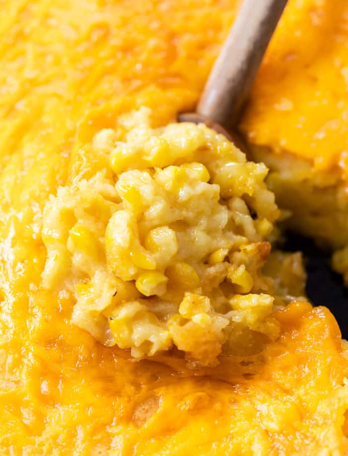 A wooden spoon scooping up Corn Casserole from a skillet.