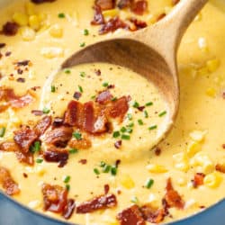 A soup pot filled with homemade Corn Chowder topped with bacon, chives, corn, and red pepper flakes.
