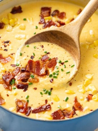 A soup pot filled with homemade Corn Chowder topped with bacon, chives, corn, and red pepper flakes.
