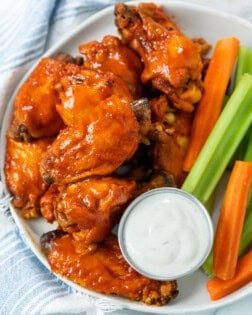 A plate with Buffalo Chicken Wings with a cup of blue cheese with celery and carrot sticks.