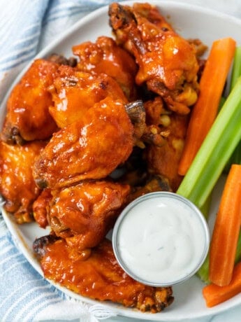 A plate with Buffalo Chicken Wings with a cup of blue cheese with celery and carrot sticks.