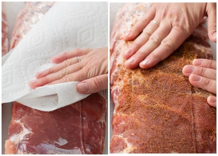 A hand patting a rack of ribs dry and working rub into the meat.