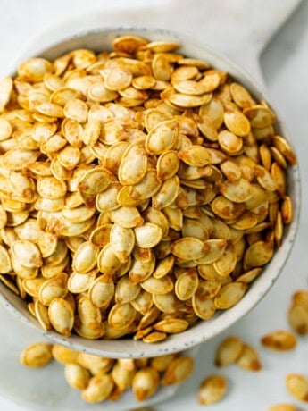 A white bowl overflowing with crispy roasted pumpkin seeds.