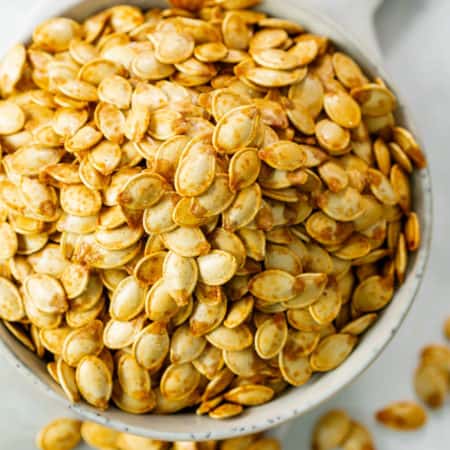 A white bowl overflowing with crispy roasted pumpkin seeds.