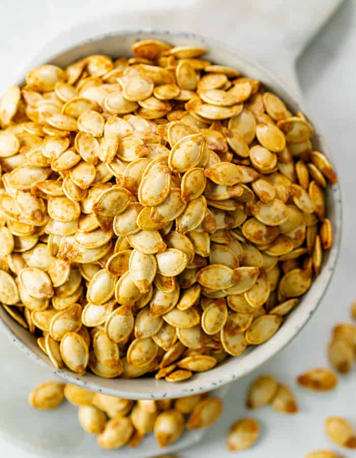 A white bowl overflowing with crispy roasted pumpkin seeds.
