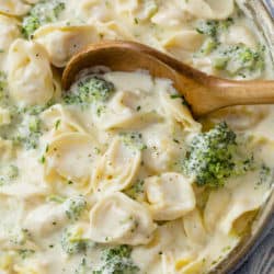 A wooden spoon in a skillet filled with Tortellini Alfredo with broccoli.