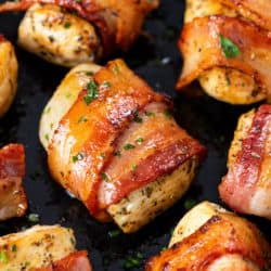 Seasoned chicken wrapped with crispy bacon in a skillet with parsley.