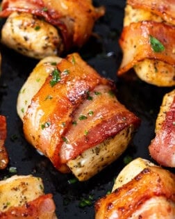 Seasoned chicken wrapped with crispy bacon in a skillet with parsley.