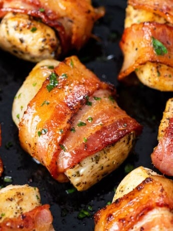 Seasoned chicken wrapped with crispy bacon in a skillet with parsley.