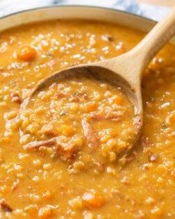 A wooden spoon scooping up ham and bean soup from a pot of soup.