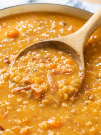 A wooden spoon scooping up ham and bean soup from a pot of soup.