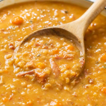 A wooden spoon scooping up ham and bean soup from a pot of soup.