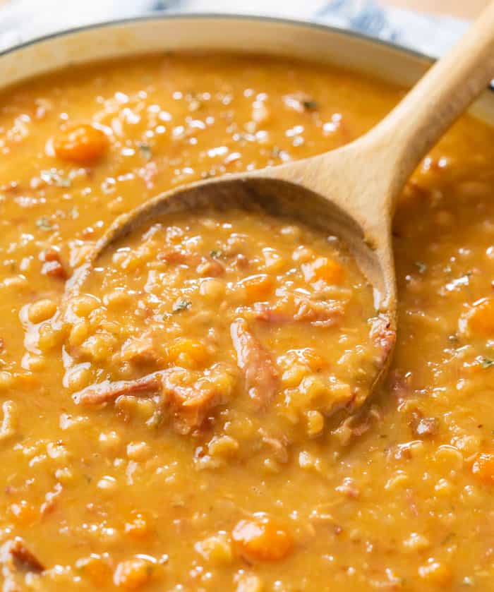 A wooden spoon scooping up ham and bean soup from a pot of soup.