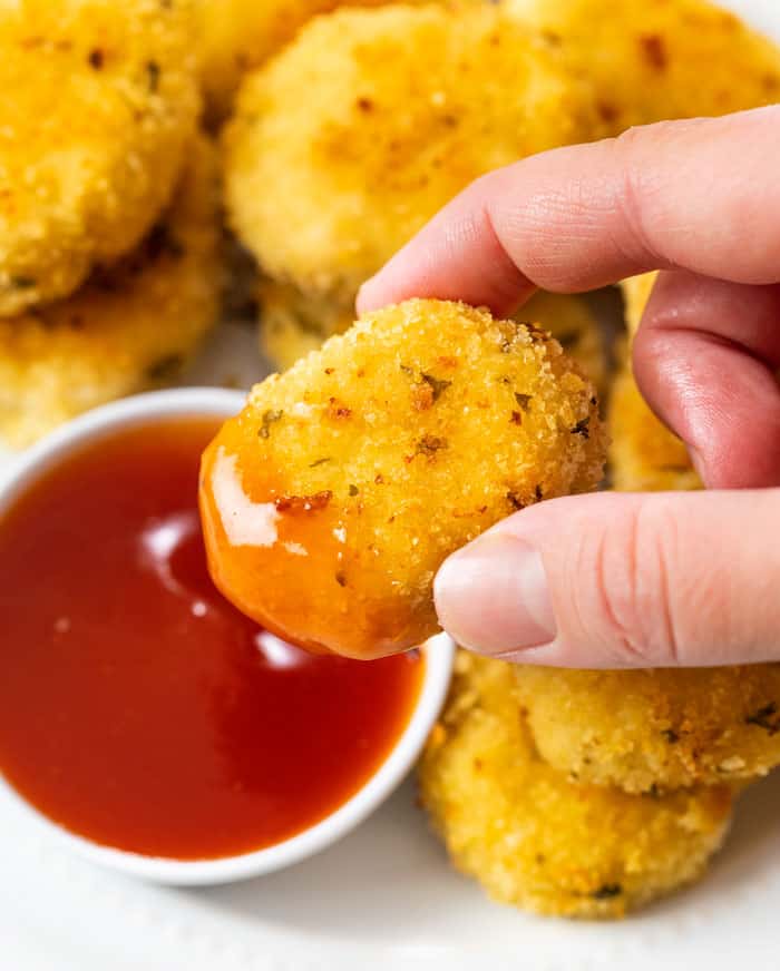 A hand holding a golden homemade chicken nugget that's been dipped in sauce.