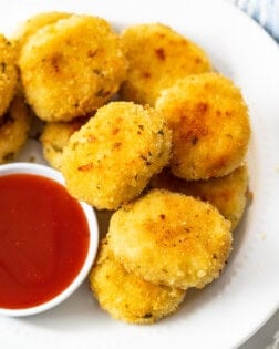 A plate of golden chicken nuggets on a white plate with sweet and sour sauce.