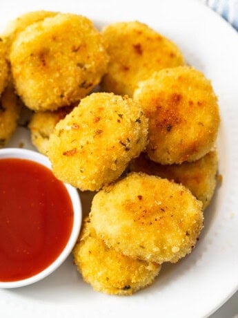 A plate of golden chicken nuggets on a white plate with sweet and sour sauce.