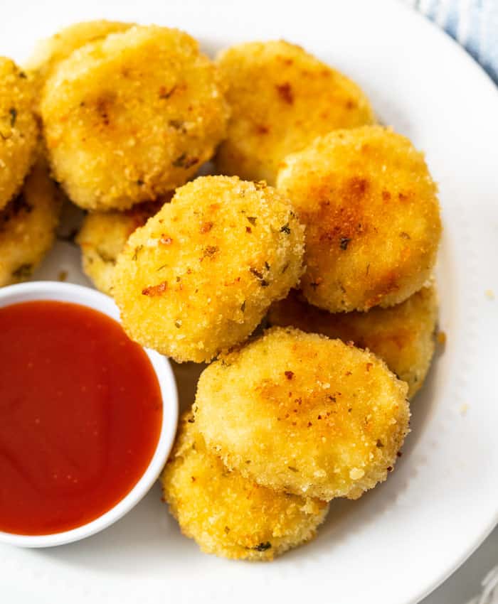 A plate of golden chicken nuggets on a white plate with sweet and sour sauce.