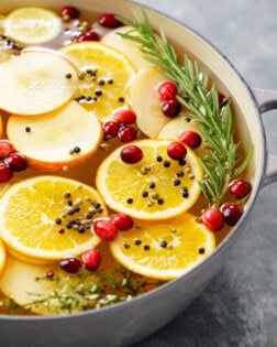 A bowl full of wet brine for a turkey with sliced fruit, fresh cranberries, and rosemary.