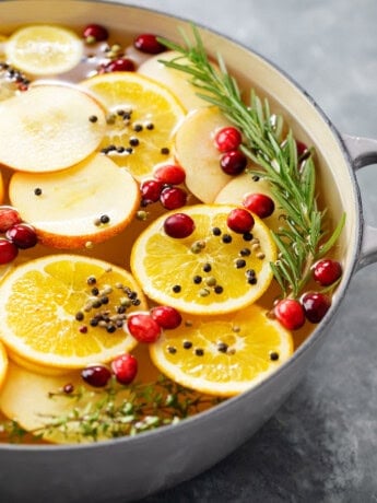 A bowl full of wet brine for a turkey with sliced fruit, fresh cranberries, and rosemary.
