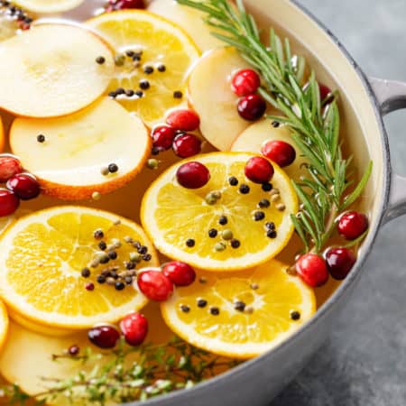 A bowl full of wet brine for a turkey with sliced fruit, fresh cranberries, and rosemary.