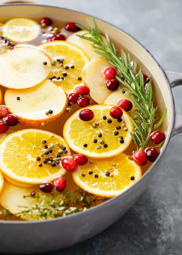 A bowl full of wet brine for a turkey with sliced fruit, fresh cranberries, and rosemary.