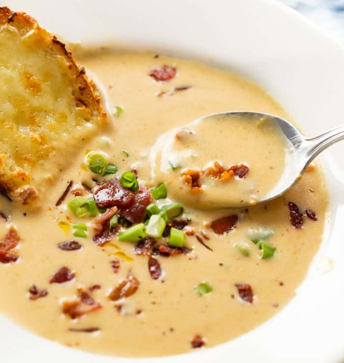 A spoon scooping up beer cheese soup from a white bowl with bacon and green onions.
