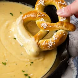 A hand dipping a soft pretzel into a skillet of Beer Cheese Dip.