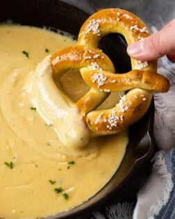 A cast iron skillet with beer cheese dip with a soft pretzel being dipped in it.