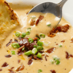 Beer Cheese Soup topped with bacon and green onions with a spoon scooping it up in the back.