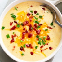 Beer Cheese Soup in a white bowl with a spoon and bacon and green onions on top.