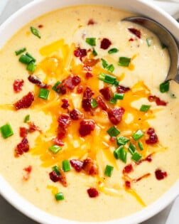 Beer Cheese Soup in a white bowl with a spoon and bacon and green onions on top.