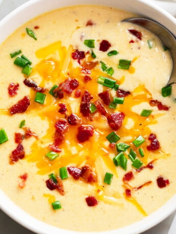 Beer Cheese Soup in a white bowl with a spoon and bacon and green onions on top.