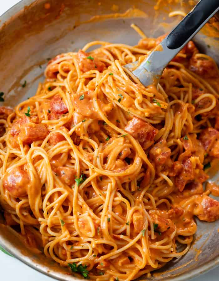 A skillet with creamy tomato pasta with kitchen tongs.