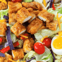 Crispy Chicken on top of a bed of lettuce with hard boiled eggs, tomatoes, cheese, and tortilla strips.