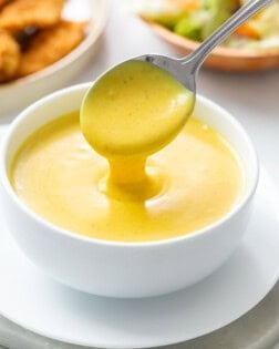 Honey Mustard in a white bowl with a spoon pouring it out.