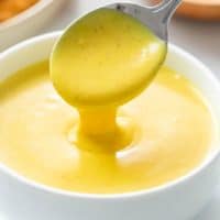 A spoon scooping up creamy honey mustard sauce from a white bowl.