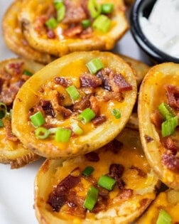 Potato Skins on a plate topped with cheese, bacon, and green onions.