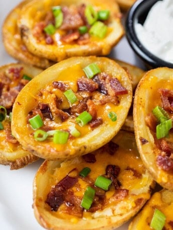 Potato Skins on a plate topped with cheese, bacon, and green onions.