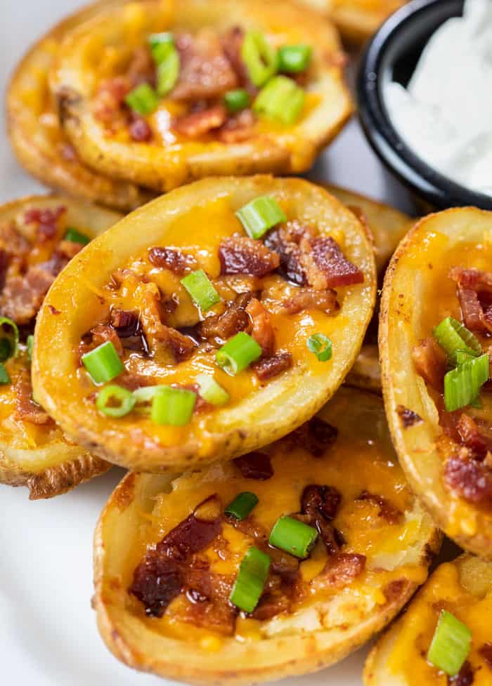 Potato Skins on a plate topped with cheese, bacon, and green onions.