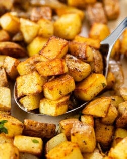 A large metal spoon full of crispy skillet potatoes.