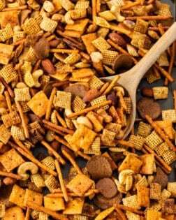 A baking sheet with spicy chex mix with a wooden spoon.