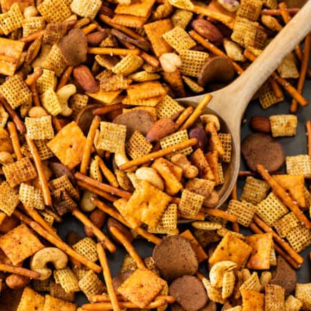 A baking sheet with spicy chex mix with a wooden spoon.