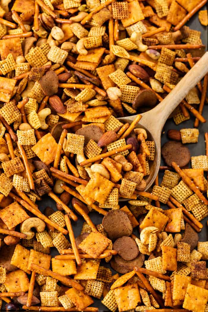 A baking sheet with spicy chex mix with a wooden spoon.