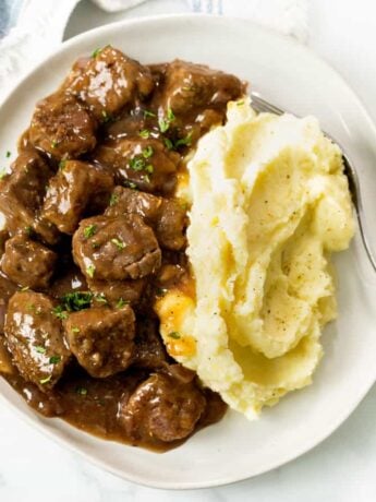 Tender Beef Tips and Gravy on a plate with Mashed Potatoes and fresh parsley.