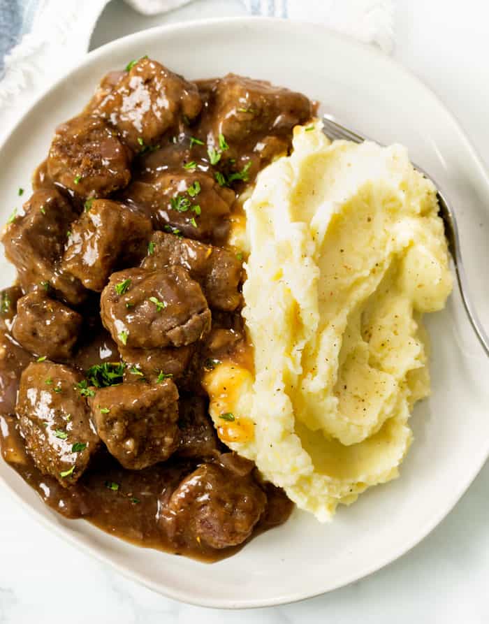 Tender Beef Tips and Gravy on a plate with Mashed Potatoes and fresh parsley.