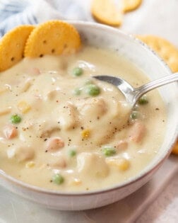 A spoon scooping up Chicken Pot Pie Soup from a bowl with crackers in the background.