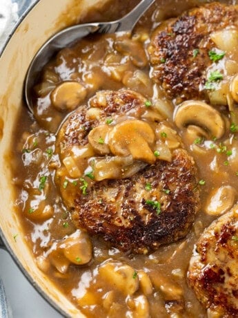 A skillet with Salisbury Steak in a thick mushroom gravy topped with fresh parsley.