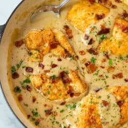 Golden Chicken Breasts in a skillet smothered with gravy and topped with bacon.